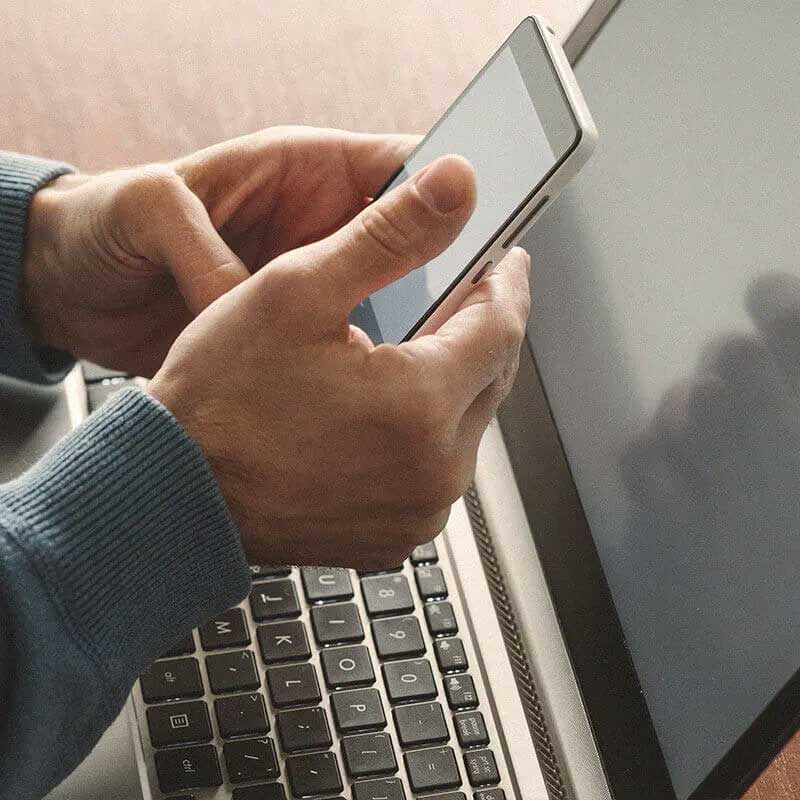 hands holding mobile phone with laptop in background